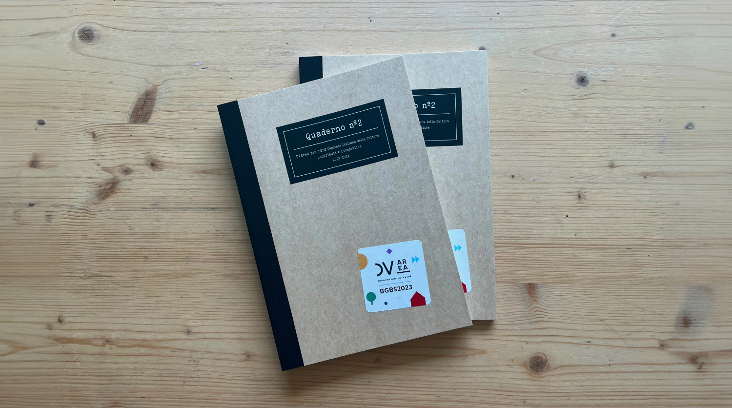 Notebook No. 2 – DVArea for BGBS2023. Two notebooks with kraft paper covers and black spines, titled "Quaderno n°2 – DVArea for BGBS Italian Capital of Culture. Contributions and Perspectives 2023–2024", placed on a light wooden table.