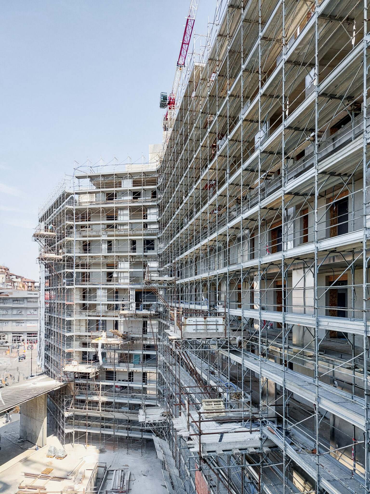 BoscoNavigli, Milan. View of a large residential building under construction with metal scaffolding covering the entire façade and a construction crane in the background, within an urban context.
