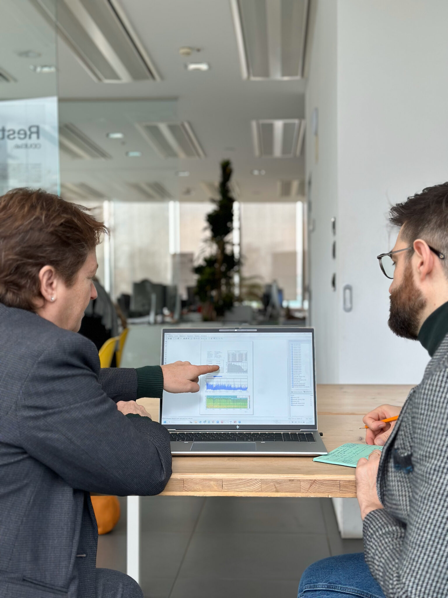 Two professionals discussing a technical analysis displayed on a laptop, with charts and data tables, in a modern office environment.