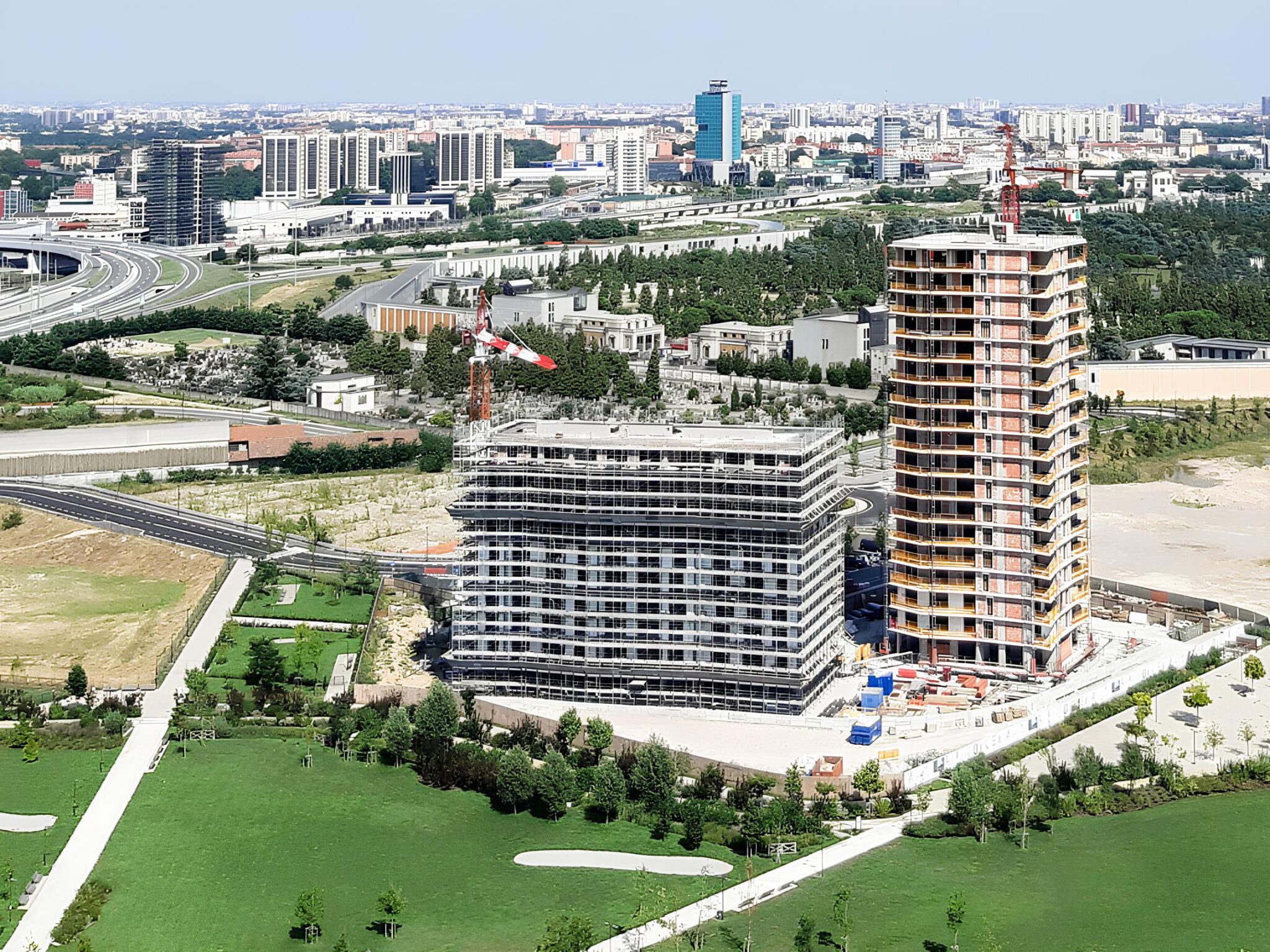 East uptown, Milano. Veduta aerea del cantiere residenziale con due torri in costruzione, circondate da aree verdi e infrastrutture urbane.