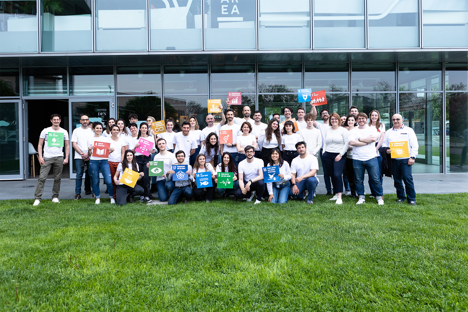 Workshop SDGs per il World Innovation Day 2023. DVArea Headquarters, Brescia. Foto di gruppo del team DVArea davanti alla sede aziendale, con cartelli degli Obiettivi di Sviluppo Sostenibile.