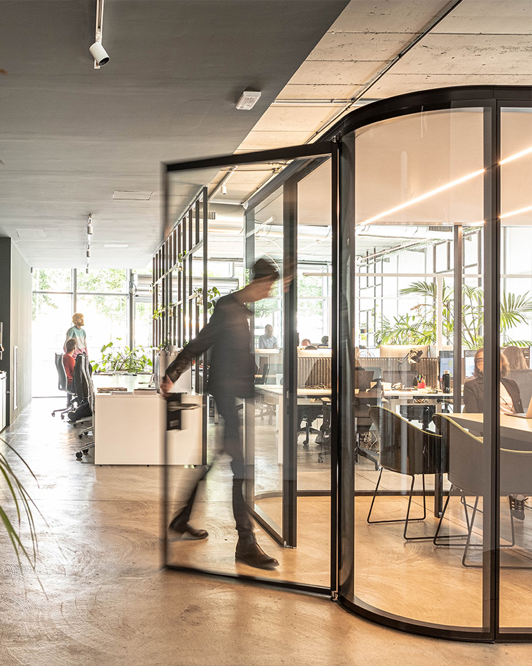 Person in motion entering a glass-walled meeting room inside a modern and bright office.