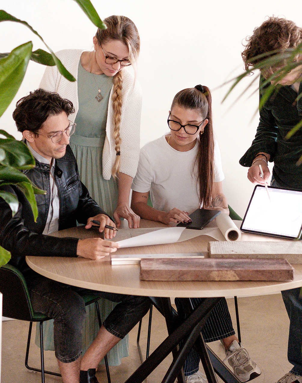 Design team working around a table with materials, drawings, and a tablet, in a bright and collaborative environment.