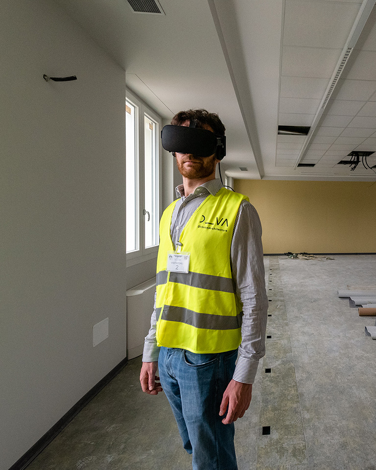 Campus Cattolica, Brescia. DVA operator during an inspection using a virtual reality headset inside a building under renovation, wearing a high-visibility vest and identification badge.