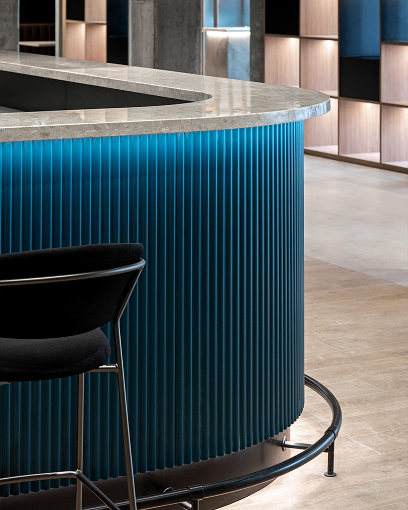 Ristopub ChorusLife, Bergamo. Close-up of a modern counter with blue ribbed cladding and marble top, featuring a black fabric and metal barstool in the foreground.